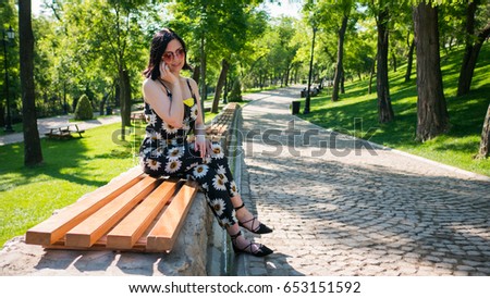 Beautiful young girl in park talking to mobile. Portrait of a happy caucasian brunette woman smiling and talking on her phone. Green background. Casual clothing. Lifestyles. 