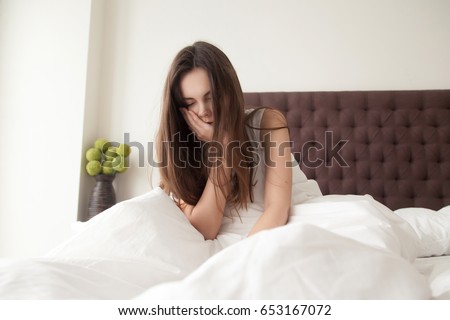 Exhausted sleepy young woman sitting in bed with messy hair, feeling drowsy after wake up too early in morning, sleepless night. Tired female teenager suffering of insomnia, lack of sleep or toothache Royalty-Free Stock Photo #653167072