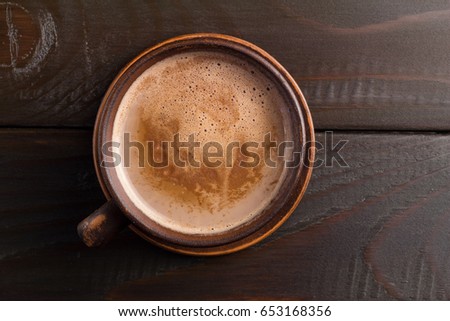Hot chocolate or cocoa drink in clay cup, on dark brown wooden table, top view.