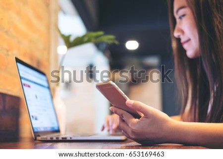 An Asian business woman holding mobile phone while using laptop on the table in office