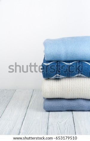 Knitted wool sweaters. Pile of knitted winter, autumn clothes on white, wooden background, sweaters, knitwear, space for text.