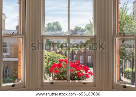 Interior of a Victorian British house with old wooden white windows  and red geraniums on the window sill facing a traditional English street Royalty-Free Stock Photo #653189086