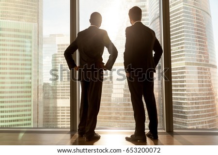 Rear view of african and caucasian businessmen wearing suits standing at full length large window enjoying great big city scenery, contemplative thoughtful multi ethnic partners building future plans Royalty-Free Stock Photo #653200072