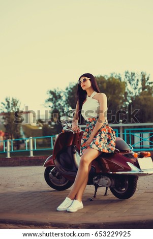 Brunette in a dress and sneakers in the street with a moped
