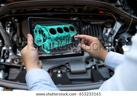 Augmented reality technology and engineering marketing concept. Hand holding tablet with AR service application to rotate 3d rendering of energy block 360 degrees with blur car engine room background Royalty-Free Stock Photo #653233165