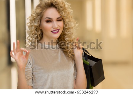close up of beautiful happy woman with shopping bags smiling and showing ok in mall. shopping concept