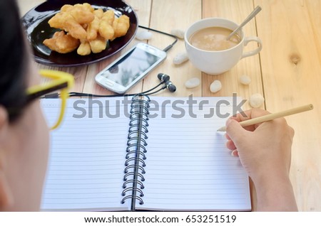 Woman caught pencil written in a book. Smart phones and breakfasts are placed on wooden floors. Ideas for work. Sunspot. Selective focus.