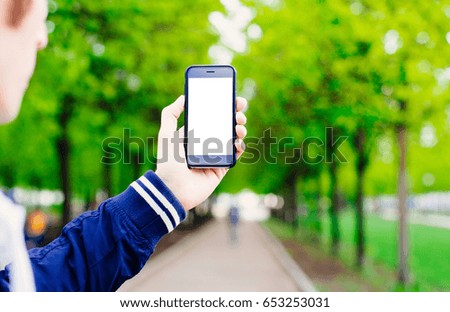 A man holding a telephone with a blank screen in the park on a background of trees, nature. Hipster using cellphone,texting or reading sms on mobile phone