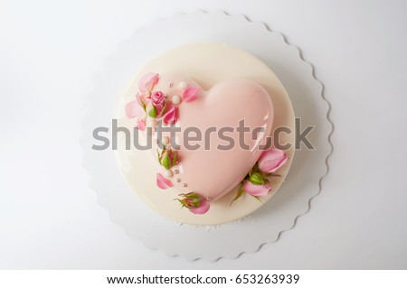 Two-tiered modern french mousse cake with pink mirror glaze in the shape of a heart decorated with roses on a white background. Picture for a menu or a confectionery catalog. Top view.