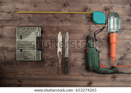 Electrical drill, tape measure, twist bits, knives and lamp on a wooden table