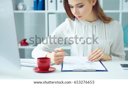Beautiful young business woman sitting at office workplace looking at the graphs. 