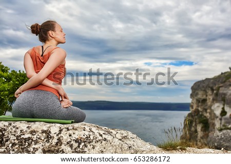 Rear view of beautiful woman doing yoga exercises on rock.