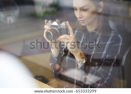 Brunette beautiful hipster girl making photo using vintage camera while spending free time indoors.Attractive concentrated woman trying to take good picture while enjoying favorite hobby in cafe