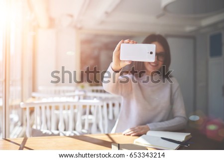 Copy space area for advertising content.Filter effect and sun flare.Selected focus on female's hand holding modern telephone while making photo and shooting video.Blurred background of young woman