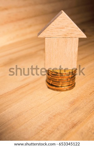 Shallow depth of field and selective focusing of a Wooden House Block stacked on gold coins with copy space for text use as background. Real Estate and Business Finance Investment concepts.