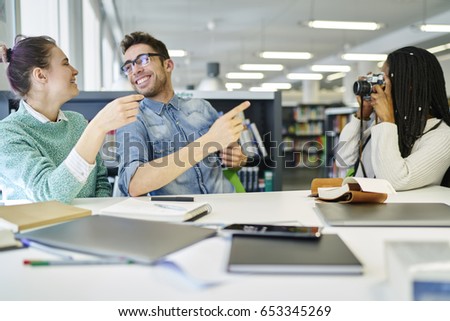 Multicultural students making funny photos on vintage camera sitting indoors during recreation time.Cheerful male and female graphic designers laughing and making pictures indoors enjoying break 