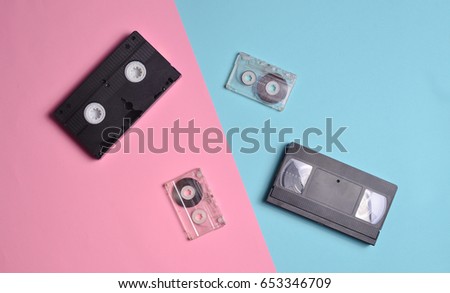 Audio cassettes and video cassettes are laid out on a multi-colored neon surface. Top view.