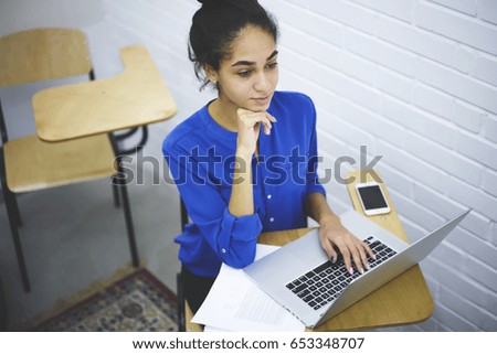 Talented good looking student carefully listening during interesting seminar in academy.Charming young woman keyboarding on laptop while sitting at wooden desk during training course in university