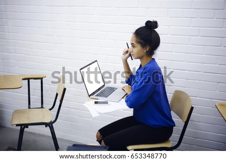 Pondering good looking female student thinking about improvements for coursework project while sitting with laptop mock up screen for your advertising content during lesson in light classroom
