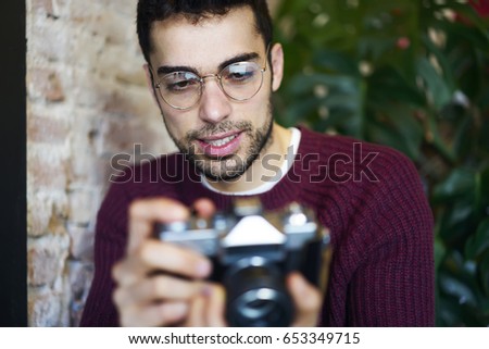 Cropped image of bearded traveller in optical eyeglasses holding vintage camera in hands and making settings to creating cool photos.Concentrated male amateour in stylish spectacles shooting video 