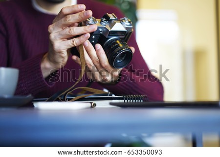 Selective focus on vintage camera with modern objective and  professional lens.Cropped image of man's hands making settings to taking pictures.Blurred background.Copy space area for advertising