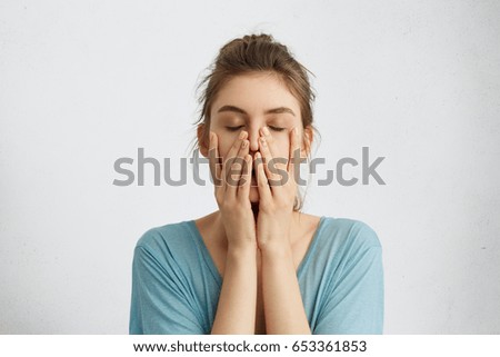 Headshot of young beautiful student female closing her eyes holding hands on chin being tired after hard work trying to relax for a minute and to gather her thoughts. Tiredness, feelings concept Royalty-Free Stock Photo #653361853