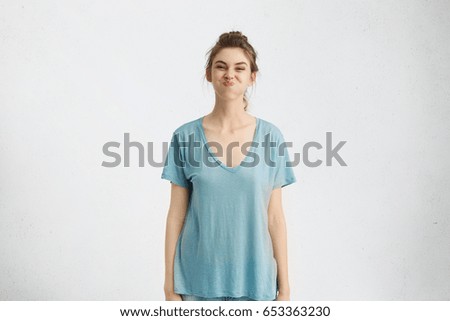 Portrait of playful funny teenage girl wearing blue t-shirt having fun indoors, holding breath, doing her best not to burst into laughter while friends trying to make her laugh. Human emotions