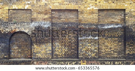 Aged brick wall with four arched bricked up windows with space for text. Royalty-Free Stock Photo #653365576
