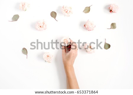 Girl's hand holding rose bud and flowers pattern made of beige roses, eucalyptus leaf on white background. Flat lay, top view. Floral background.