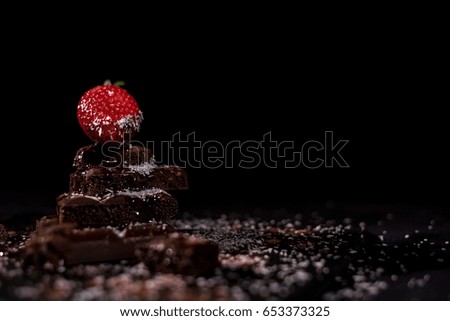 One red straberry on a dark  chocolate and black background with coconut chips