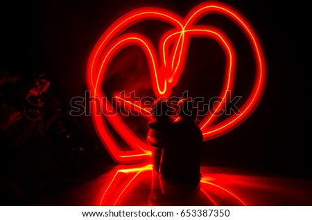 Two young lovers paint a heart on fire. Silhouette of couple and Love words on a dark background. Love concept