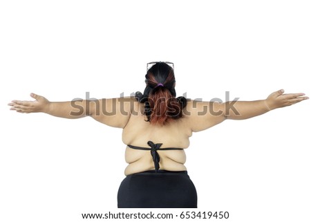 Back view of obese woman standing in the studio while wearing a black bikini and raising hands, isolated on white background