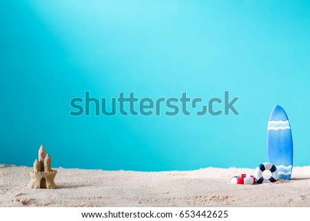 Summer theme with surfboard and sand castle on a bright blue background Royalty-Free Stock Photo #653442625