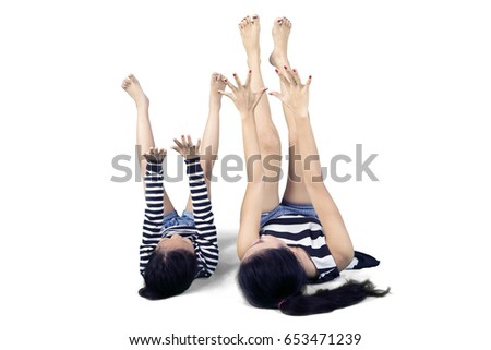 Image of young mother lying on the floor with her daughter while exercising together in the studio