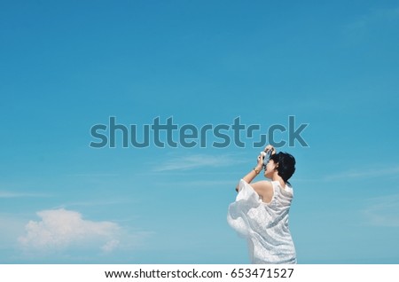 Asian woman holding camera with copy space on blue sky background 