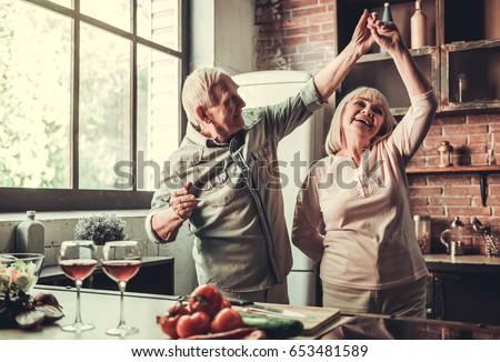 Beautiful senior couple is dancing and smiling while cooking together in kitchen Royalty-Free Stock Photo #653481589