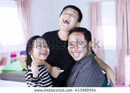 Picture of a happy family is painting on a face to each other while laughing together in the bedroom