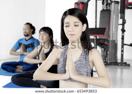 Picture of a beautiful trainer meditating in a yoga pose with her clients while sitting in the fitness center