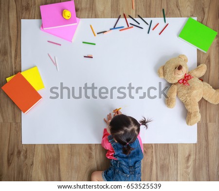 Little Asian girl drawing with colors pen in paper on floor indoors at home, top view with copy space