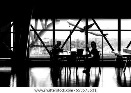 Silhouette of man working on laptop with woman using cell phone with airplane taking off social distancing concept
