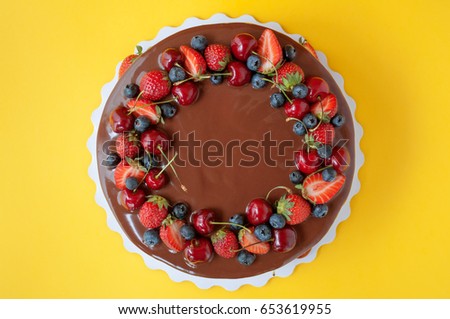 Birthday cake in chocolate with strawberries, blueberries and cherry on yellow background. Top view. Picture for a menu or a confectionery catalog.