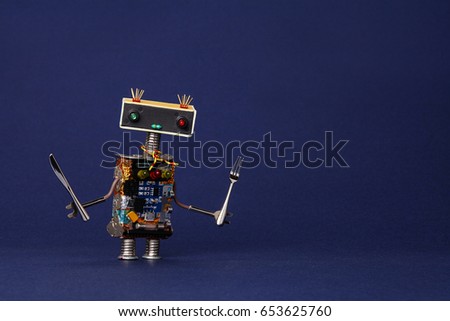 Friendly robot waiter with fork and knife. Food menu concept cute cooking kitchen chef toy character on dark blue textured paper copy space.