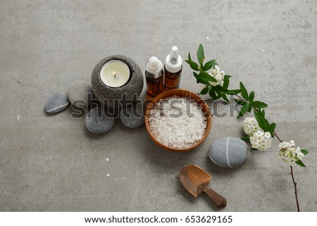 spa setting with white flowers, candle ,salt in bowl,stones ,oil on gray background