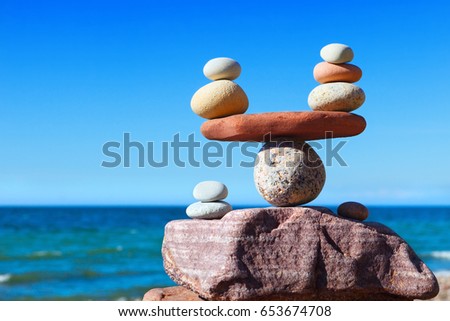 Symbolic scales of stones against the background of the sea and blue sky. Concept of harmony and balance. Pros and cons concept. Royalty-Free Stock Photo #653674708