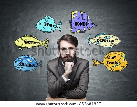 Portrait of a confident bearded businessman wearing a brown suit and sitting near a blackboard with business buzzwords written on fish of different colors.