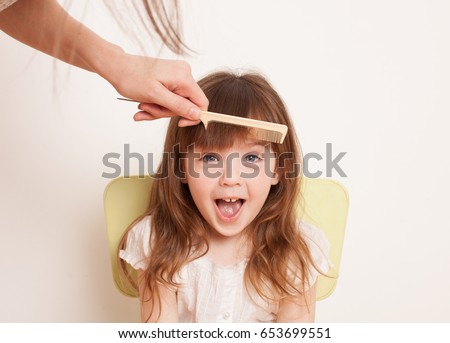 Woman's hand combing her bangs for a little girl. The daughter shouts. Close-up. Royalty-Free Stock Photo #653699551