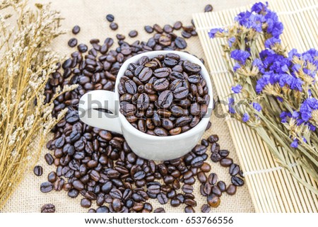 Coffee beans in white cup with dry flower on sack background