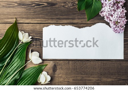 Wooden background of brown color with a clean sheet in the center and flowers on the sides. greeting note