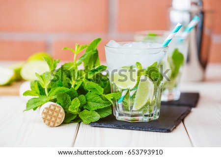 Two fresh mojitos cocktail in glass on wooden table. Mojitos with mint leaves, lime and ice. Drink making tools and ingredients for cocktail.