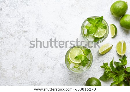 Mojito cocktail alcohol bar long drink traditional Cuba fresh tropical beverage top view copy space two highball glass, with rum, spearmint, lime juice, soda water and ice on white concrete table. Royalty-Free Stock Photo #653815270